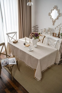 Close-up of beige linen tablecloth featuring delicate white fringe tassels on wood table