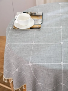 Detail of grey linen plaid tablecloth with white embroidery and beige fringe tassels