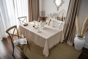 Close-up of beige cotton linen tablecloth with ball fringe trim in a rustic home setting