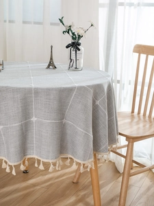 Detail of grey round tablecloth with white grid patterns and elegant cream tassels