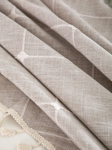 Close-up of beige linen tablecloth featuring white lattice embroidery and tassel fringe