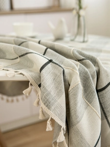 Close-up of woven plaid tablecloth with grey-white pattern and cream tassel fringe