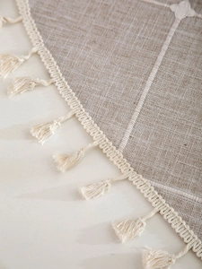 Detail of linen coffee tablecloth featuring white embroidery and elegant cream tassels