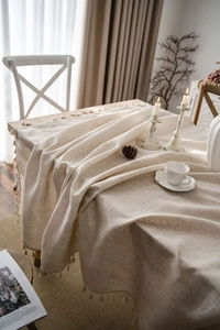 Detailed close-up of beige linen tablecloth fabric with elegant fringe tassels in a rustic home