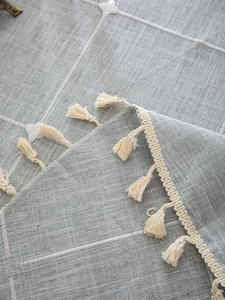 Detailed close-up of grey linen tablecloth featuring white check pattern and tassels