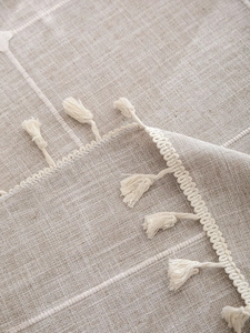 Close-up of beige linen tablecloth with white grid pattern and elegant fringe tassels