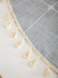 Detail of grey linen-style tablecloth with white embroidery and cream fringe tassels