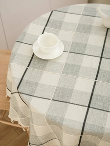 Detailed view of grey checkered linen tablecloth with decorative fringe on a round table