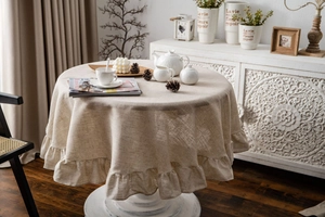 Close-up of beige linen round tablecloth with elegant ruffle hem in a vintage room