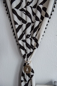 Detail of minimalist curtain with black geometric print, fringe tassels, and wooden elk pendant