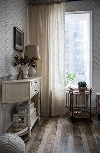 Detail view of light beige linen curtains with a classic side table and woven cart