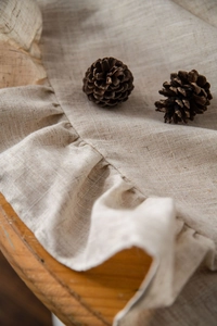 Close-up detail of natural linen tablecloth with ruffle edges and decorative pine cones