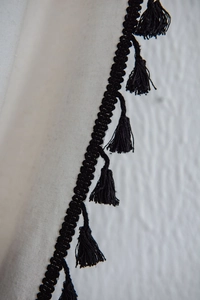 Close-up of black fringe tassel trim on white minimalist cotton linen window curtain fabric