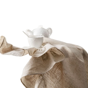 Elegant white embossed ceramic tea set with teapot and cup on ruffled linen tablecloth
