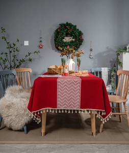 Close-up of red festive tablecloth featuring wave jacquard patterns and white cotton tassels