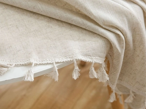 Detail of beige cotton linen tablecloth with elegant tassels and natural fabric texture
