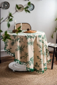Detailed texture of cotton linen round tablecloth featuring green pine branch prints and tassels