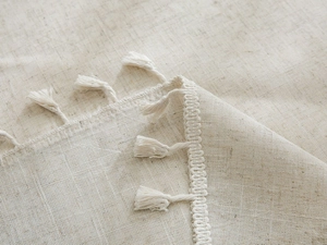 Macro detail of beige linen tablecloth fabric showing natural texture and tassel fringe