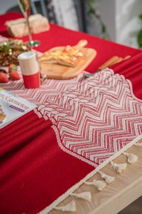 Detail of red table runner with wave jacquard pattern and white fringe on wooden table