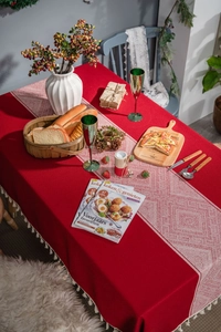 Détail d'une nappe rouge à pompons avec chemin de table aux motifs géométriques ethniques