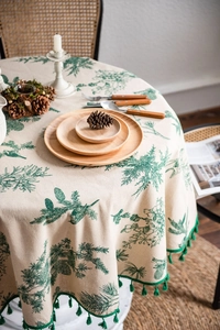 Detail view of round cotton linen tablecloth with green pine branch prints and tassel edges