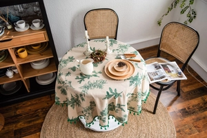 Detail of round beige tablecloth with green pine needle prints and ball fringe trim
