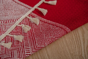 Détail de nappe jacquard rouge avec motifs géométriques et franges à glands blanc cassé
