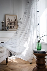 Detail of white sheer curtain featuring black horizontal stripes and stylish tassel trim