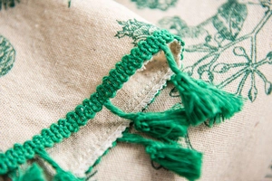 Close-up of green pine branch print cotton linen tablecloth with handmade fringe trim