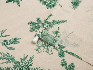 Detailed close-up of green pine needle print on beige linen curtain fabric with hemmed edge