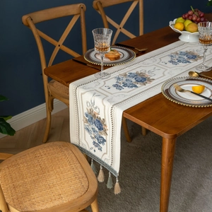 European jacquard table runner with blue floral embroidery and tassels on a dark wood table
