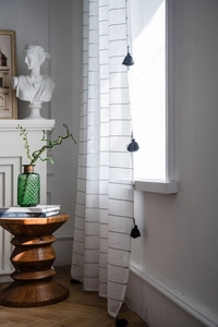 Detail of white striped sheer curtain with black tassels in minimalist home setting