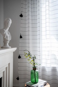 Close-up of white semi-transparent striped curtain with black tassel fringe detail