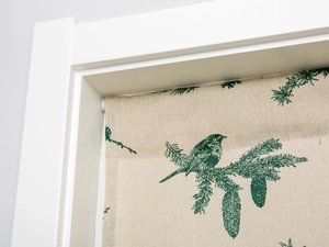 Detail of linen door curtain with green pine branches and bird print in white frame