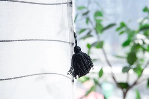 Close-up of black tassels on white striped semi-sheer curtains with modern minimalist design