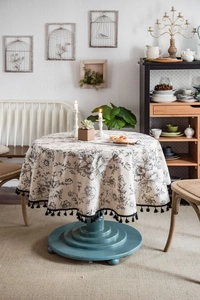 Detail of round cotton linen tablecloth with black floral print and fringe edges