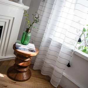 Modern semi-sheer white striped curtains with black tassels in a minimalist interior setting