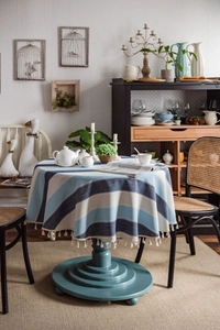 Detailed close-up of blue striped tablecloth with elegant cream fringe on a wooden table