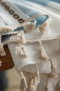 Makrodetail eines Boho-Tischläufers mit blauer Stickerei und beigen Quastenverzierung