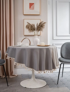 Close-up of grey jacquard round tablecloth with cream cotton tassels and premium drape