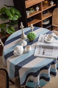 Detail of blue striped cotton linen tablecloth featuring decorative cream tassels