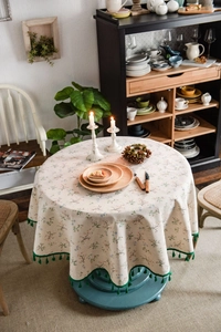 Detail of floral round tablecloth featuring green tassel fringe and rustic beige fabric