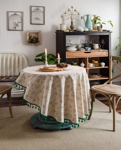 Detail of round cotton linen tablecloth featuring floral prints and green tassel edges