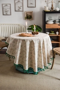 Detail of floral cotton linen tablecloth featuring green fringe tassels on a round table