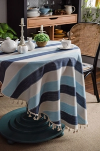 Detailed view of blue striped tablecloth with ivory woven tassels on a round dining table
