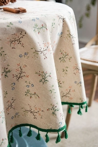 Detail of floral linen tablecloth featuring green tassels and rustic flower patterns