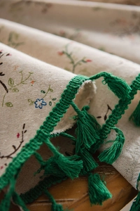 Detail of floral embroidery on beige linen tablecloth with green fringe tassels