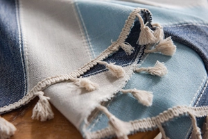 Detail shot of woven blue and beige striped tablecloth texture with tassel fringe on wood