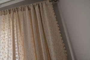 Close-up of beige cotton linen curtain with white daisy floral print and tassel trim