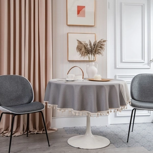 Elegant grey round tablecloth with white tassels on a dining table in modern interior